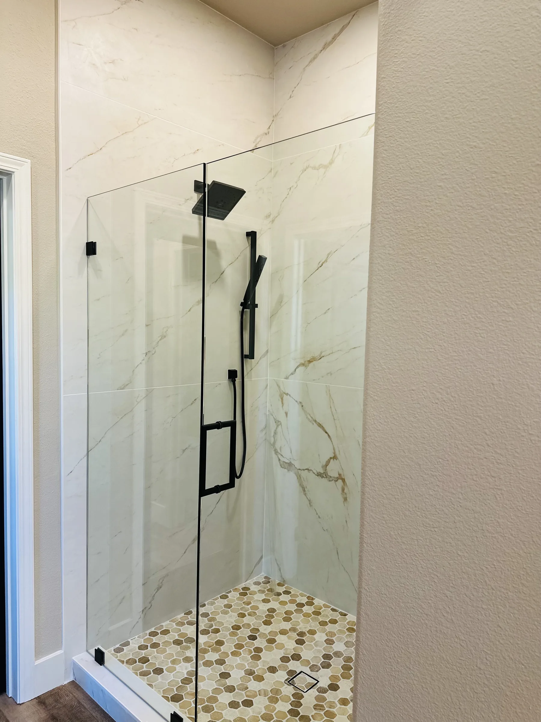 Frameless glass walk-in shower with marble tile and matte black fixtures