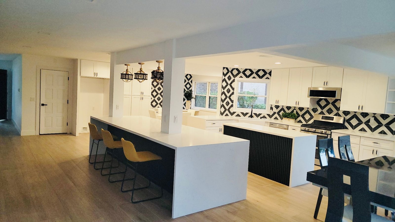 Open kitchen remodel with long quartz waterfall bar, fluted black island, and geometric black-and-white tile