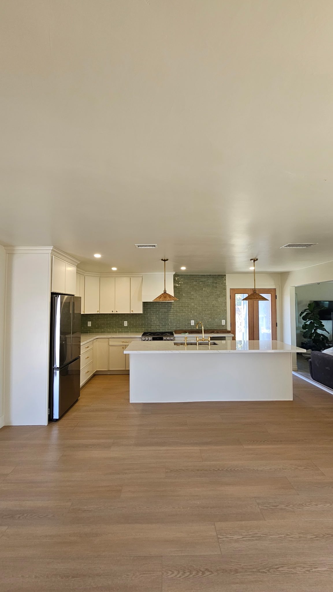 Kitchen remodel with green tile backsplash, quartz island, and brass pendants